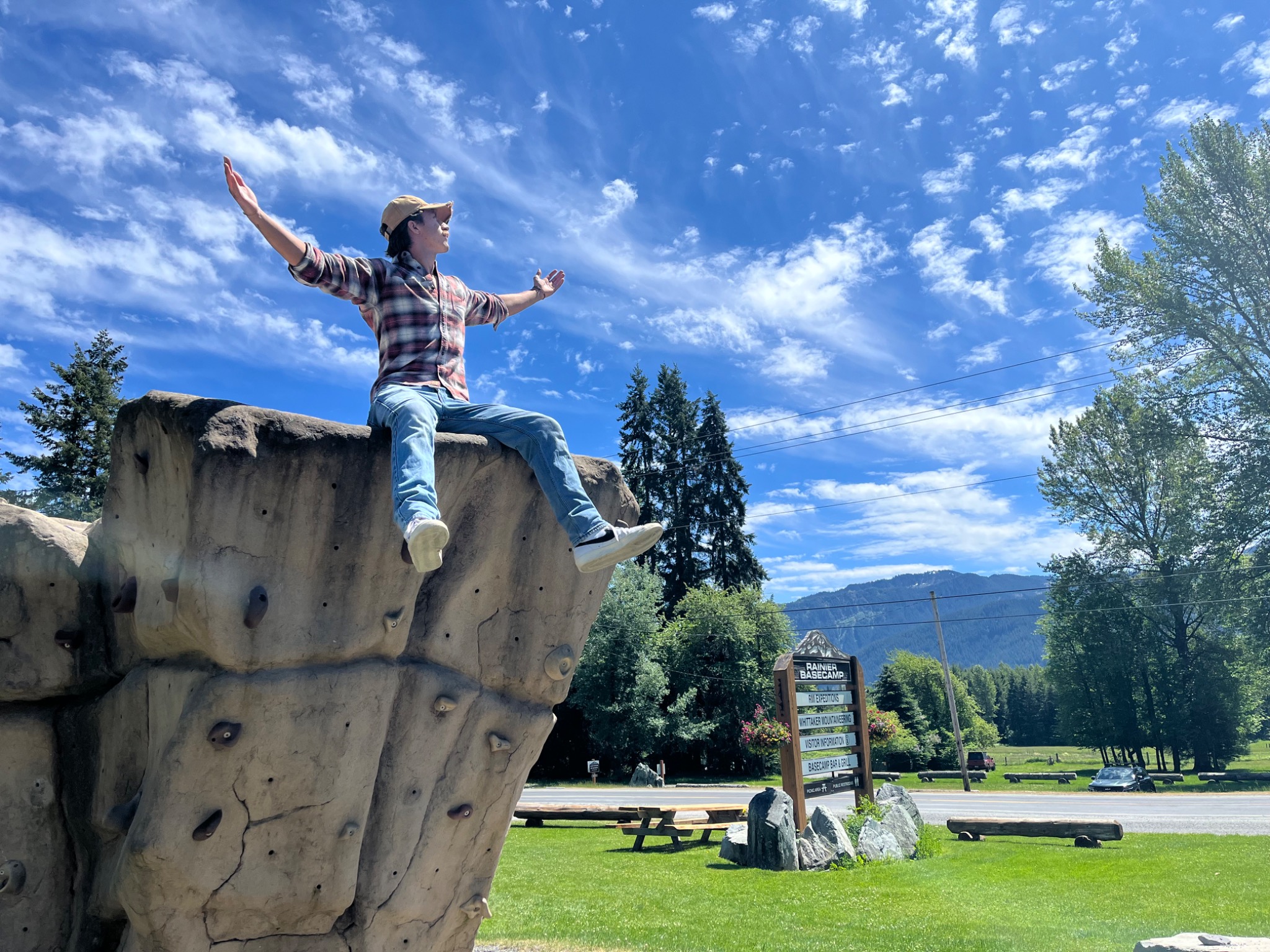 A man sitting on a climbing wall with his arms open beneath a vivid blue sky