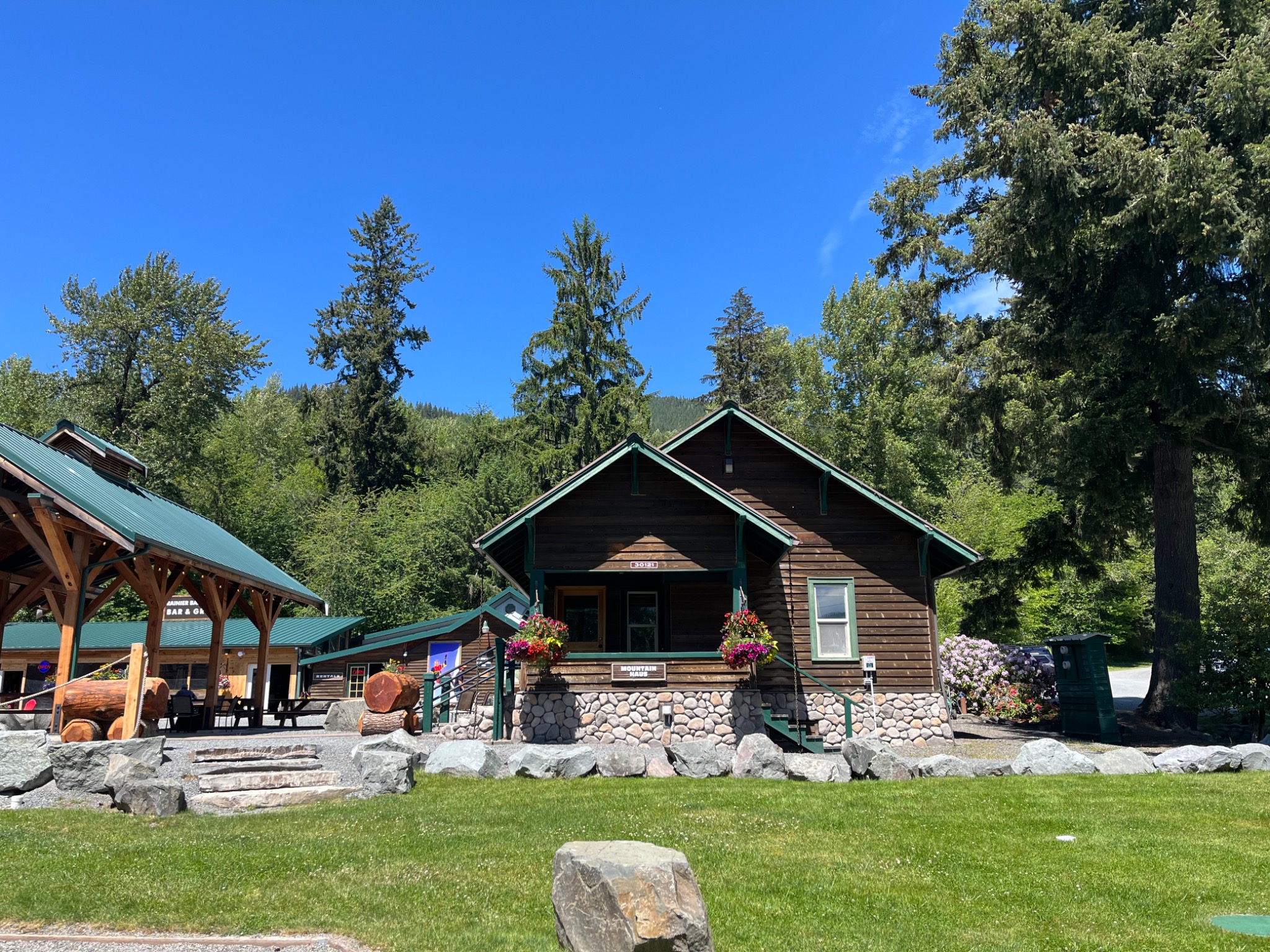 A wooden mountain lodge framed by trees and a bright blue sky