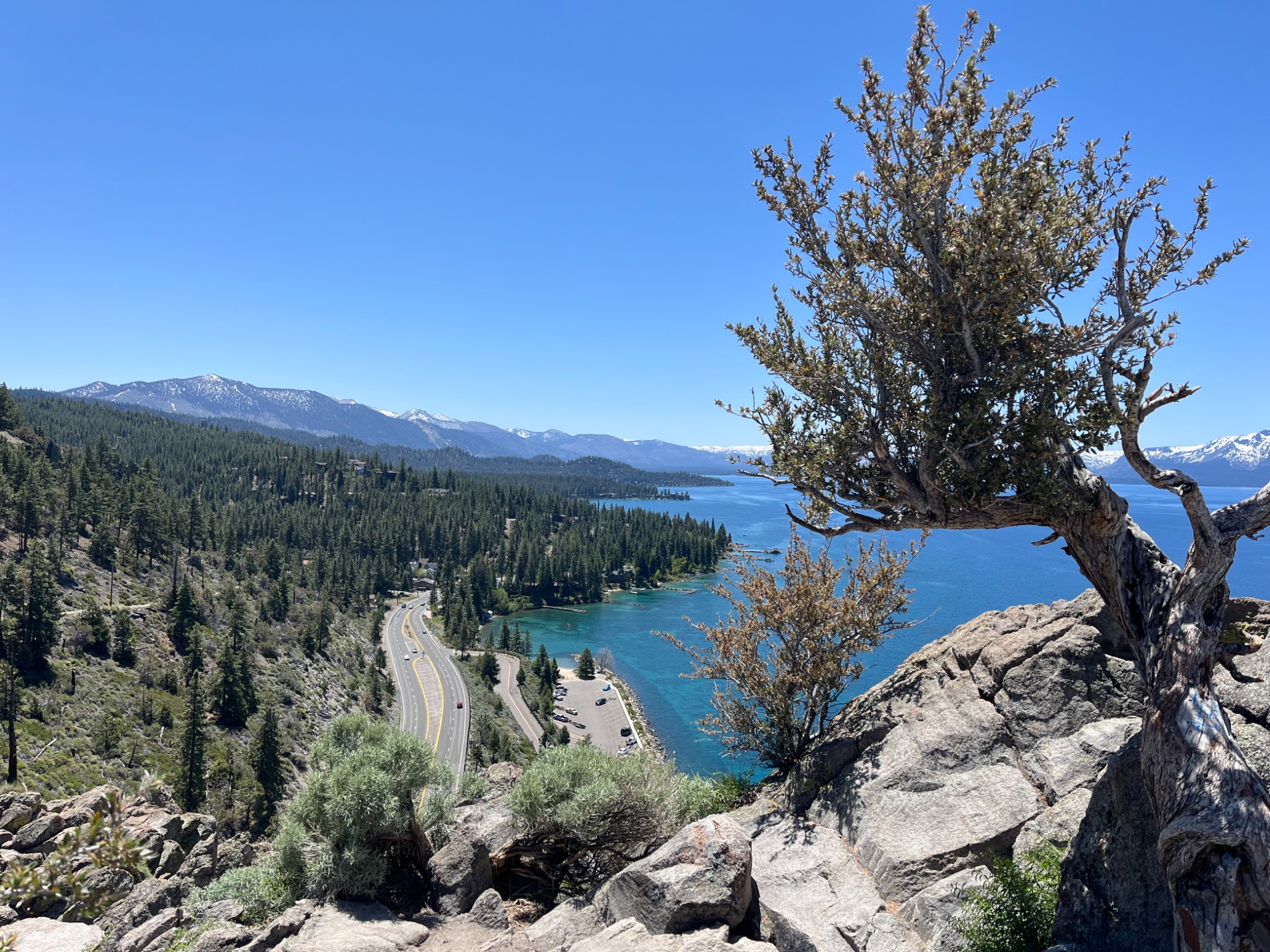 A panoramic overlook of Lake Tahoe, mountain roads, rocks, and trees